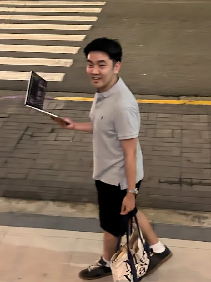 Jan Benjamin Yap walking down a street at night, holding an open laptop in one hand